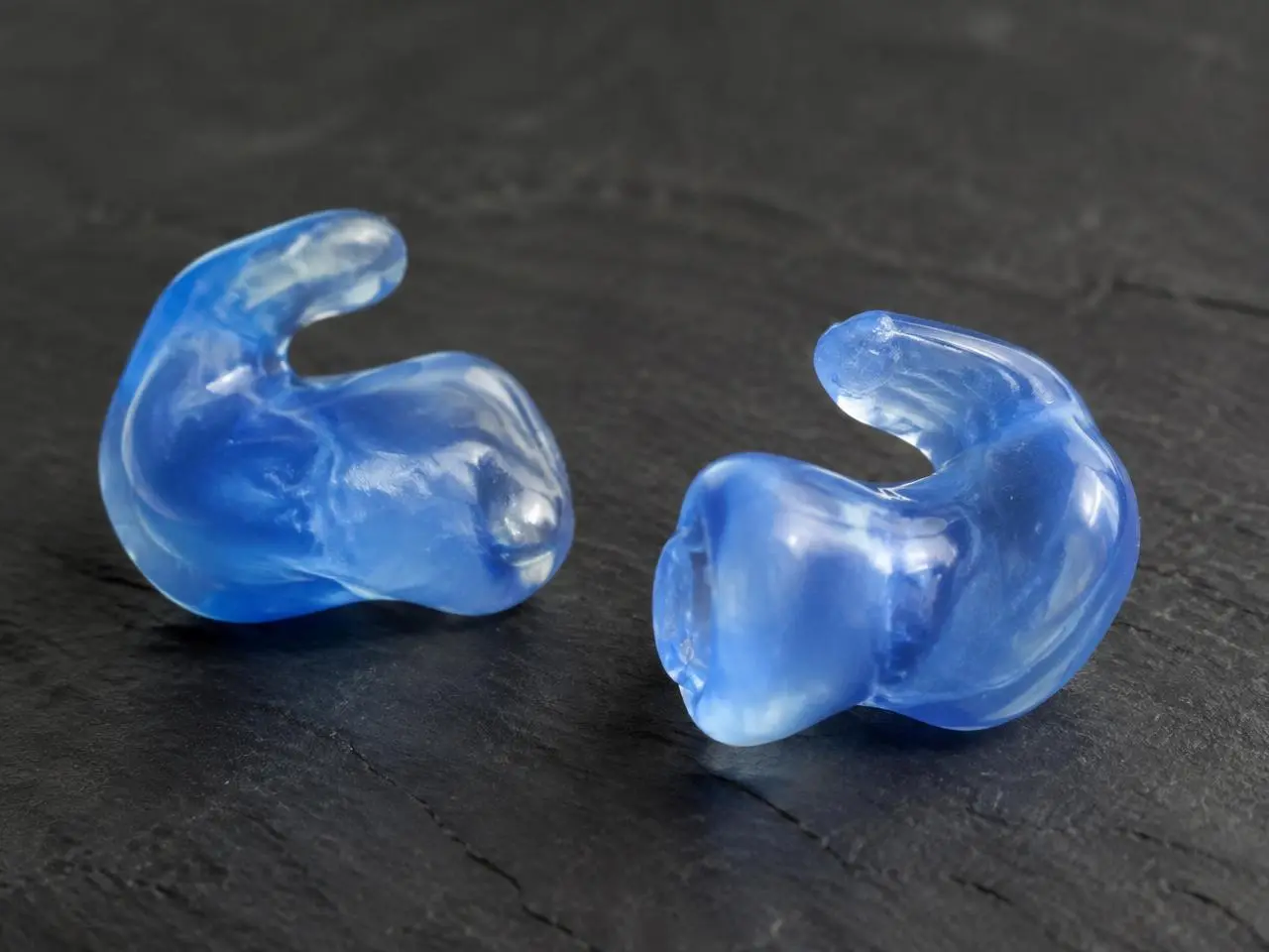 Zwei maßgefertigte blaue Otoplastiken auf dunklem Schiefer